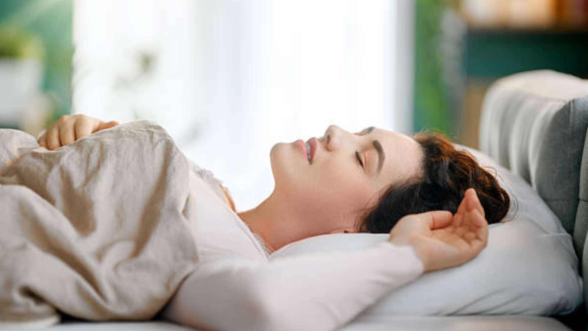 Woman lying in bed practicing breathwork with a calm expression and soft lighting